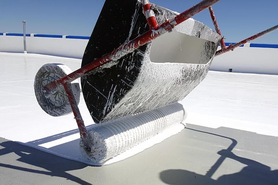 Silicone roof coatings being applied with a tank spreader, ensuring even coverage and enhanced weather resistance for long-term roof protection.