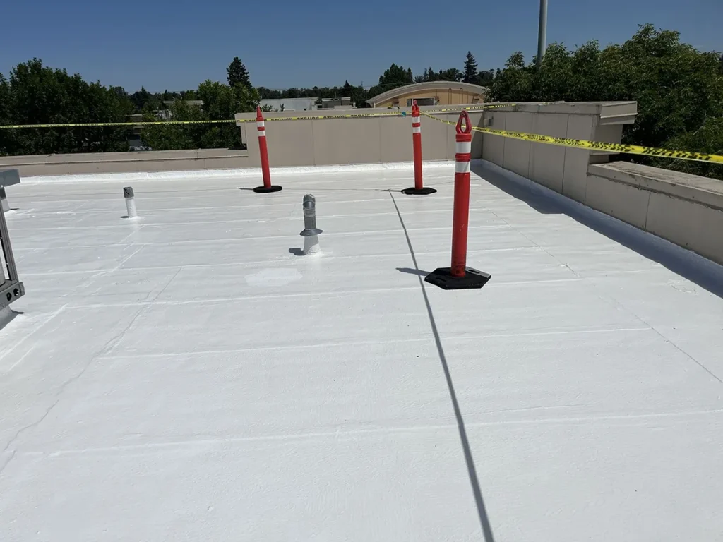 On-the-roof image of commercial flat roof with Envir-O-Sil high-solids silicone top coat and warning flags marking the perimeter of the roof.