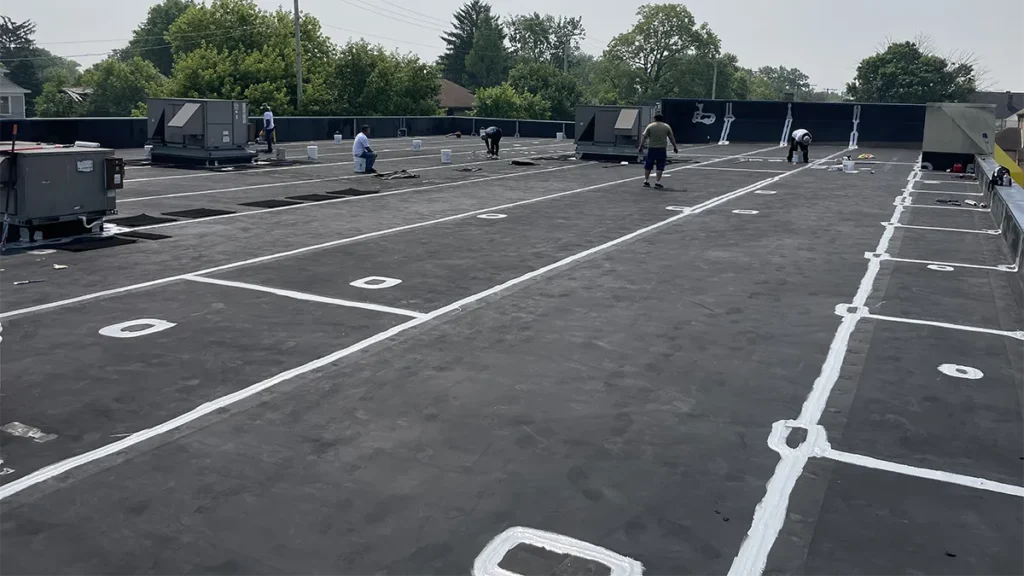 Workers treating seams and other details with thick waterproofing sealant in preparation for silicone coating.
