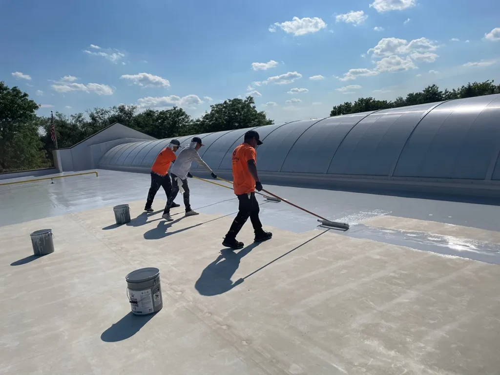 Workers roll-applying high-solids silicone coating to commercial flat roof.