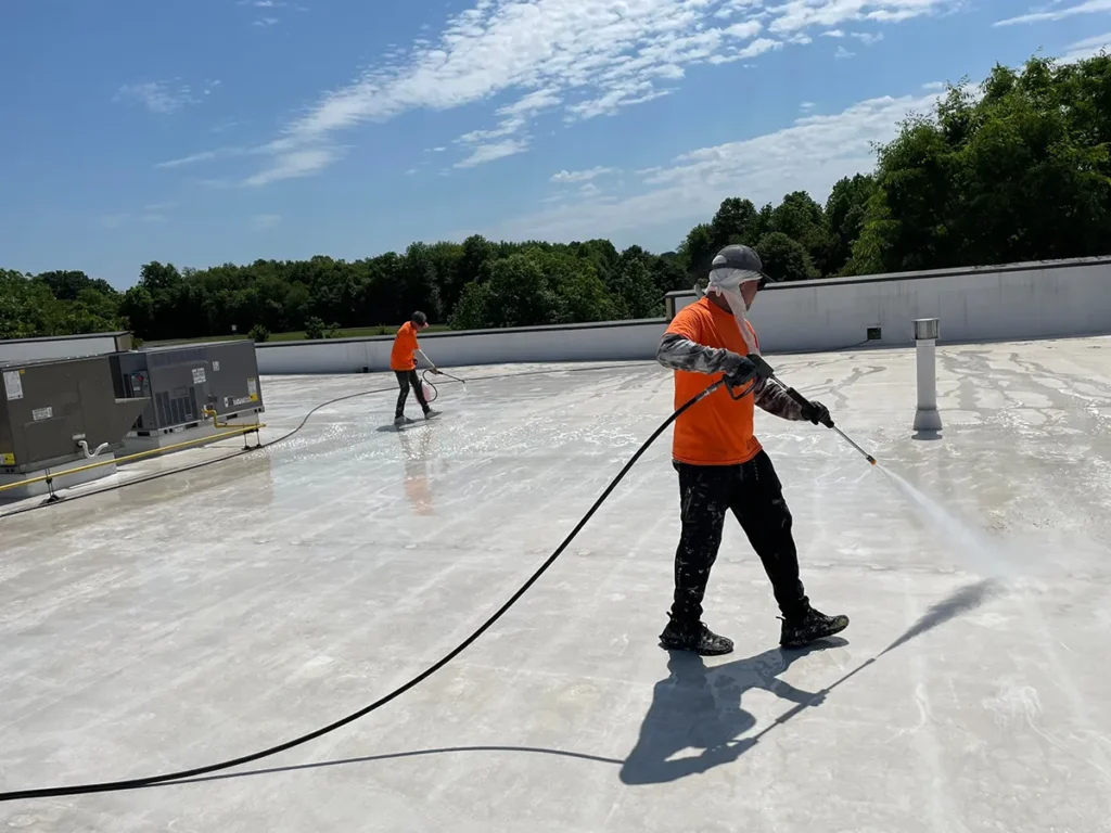Two workers pressure-washing commercial flat roof in preparation of Envir-O-Sil coating application.