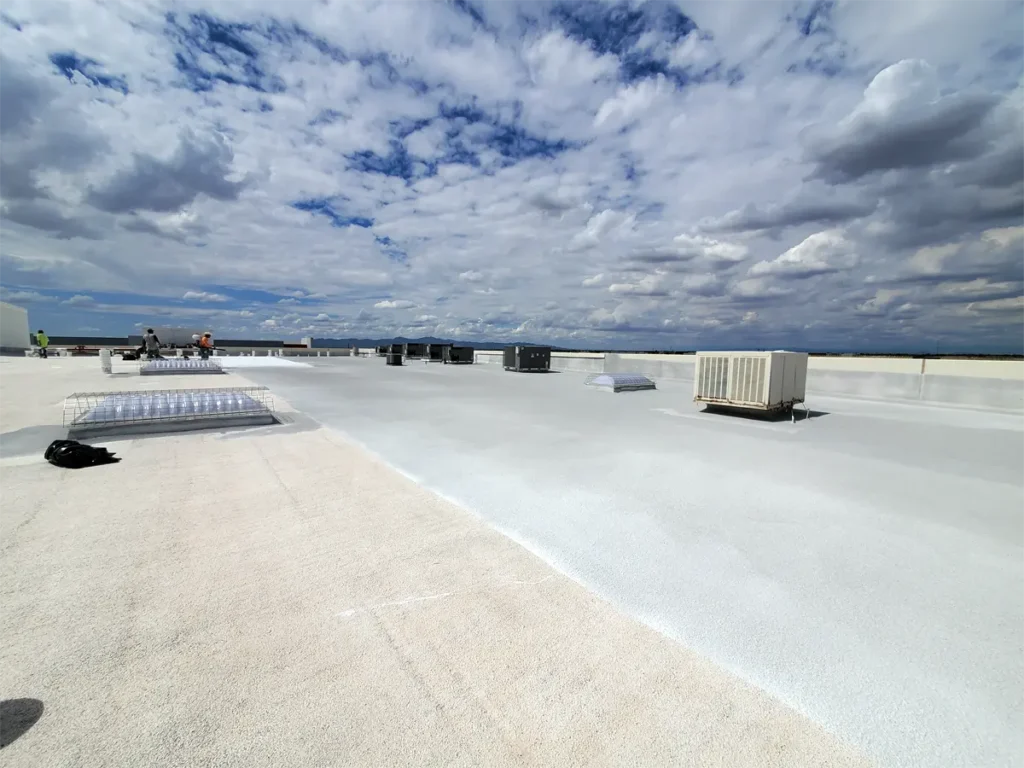 Spray foam system top coat being applied to a commercial flat roof, providing a protective, durable finish for enhanced weather resistance and longevity.