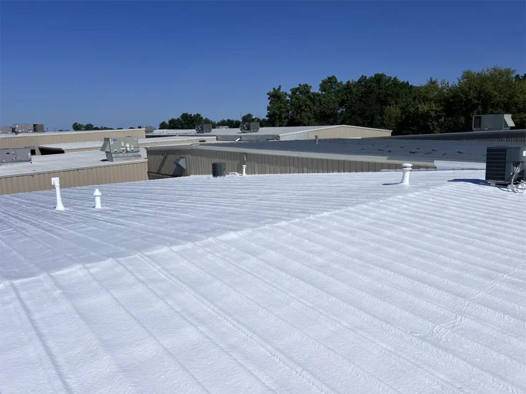 Spray foam system applied over an industrial metal roof, creating an insulating layer that improves energy efficiency and weather resistance.