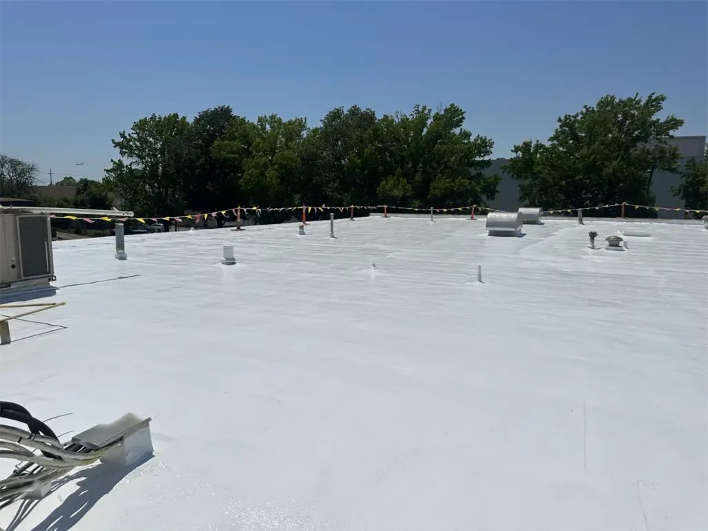 Current installation of a spray foam system over a commercial flat roof, with a safety line around the perimeter to ensure worker safety during application.