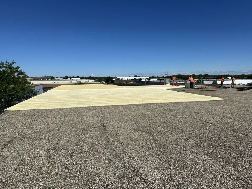 Contractors spraying foam on a commercial roof, being installed over a granulated surface for enhanced durability and weather protection.
