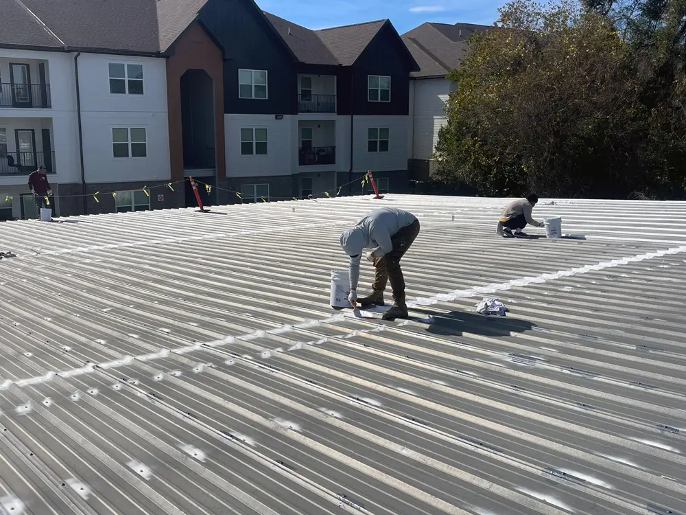 Applicators waterproofing seams, fasteners, and other details with Acrylic Brush-Grade 220 on a commercial metal roof.