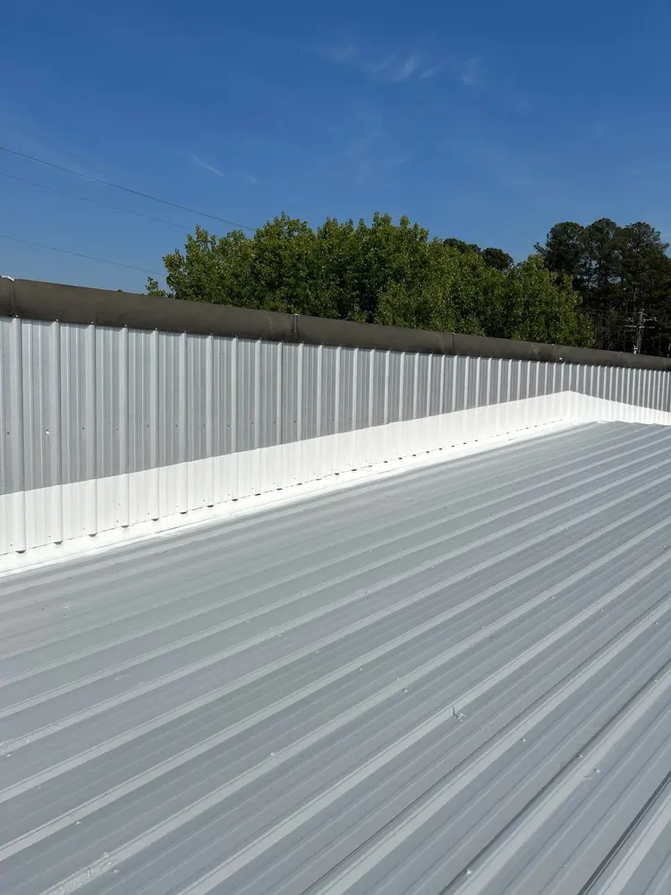 View of mastic application (Acrylic Brush-Grade 220) on wall-to-roof transition on large commercial metal roof.