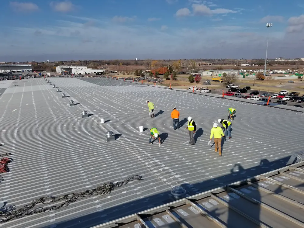 Overhead view of workers applying mastics (Acrylic Brush-Grade 220, Acrylic Butter-Grade 221) to roof details, showcasing meticulous sealing and waterproofing.
