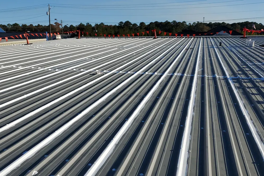 On-roof view of a metal roof showing waterproofed seams and fasteners sealed mastics (Acrylic Brush-Grade 220, Acrylic Butter-Grade 221), highlighting precise application for enhanced protection.