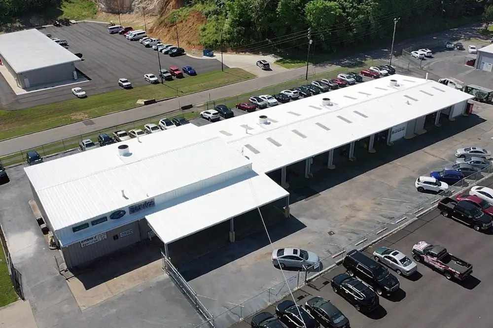 Aerial view of an automotive repair building featuring a restored metal roof coated with the Met-A-Gard system (Acrylic 211 top coat), showcasing its reflective and durable finish.
