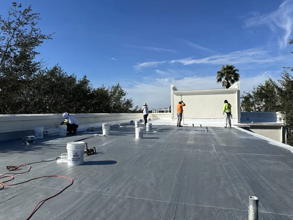 Roof coating contractors applying Ure-A-Sil California high-solids silicone top coat over low-VOC urethane base coat on flat roof of retail building.