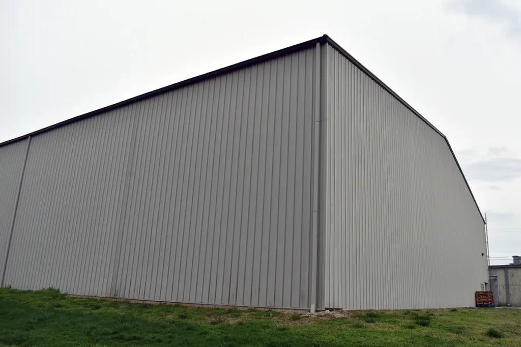 A large building with coated metal siding, grass, and a cloudy sky