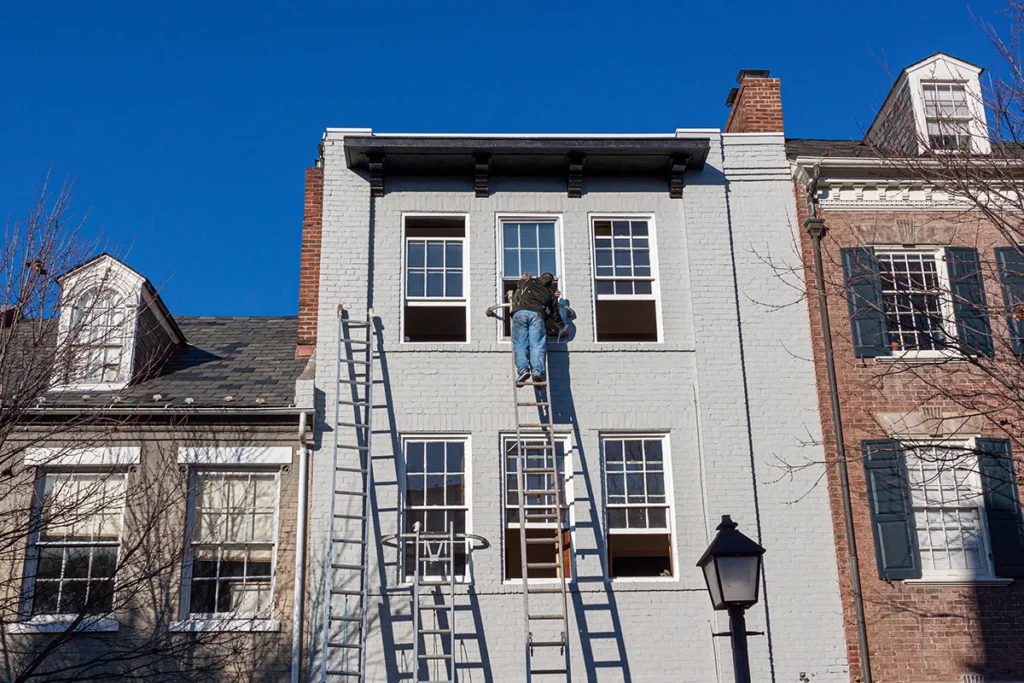 Contractor detailing around windows of Wall-Coat application system on old brick building.