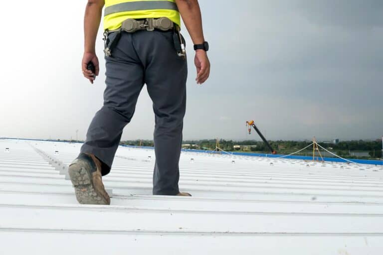 Technician walking on a commercial metal roof with a walkie-talkie, conducting an inspection as part of routine maintenance best practices to identify potential issues and ensure the roof's longevity.