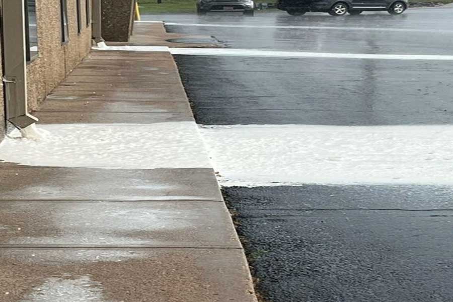 Wash-off of roof coating from a commercial roof, with runoff spilling into the parking lot, highlighting the need for proper drainage and containment during maintenance.