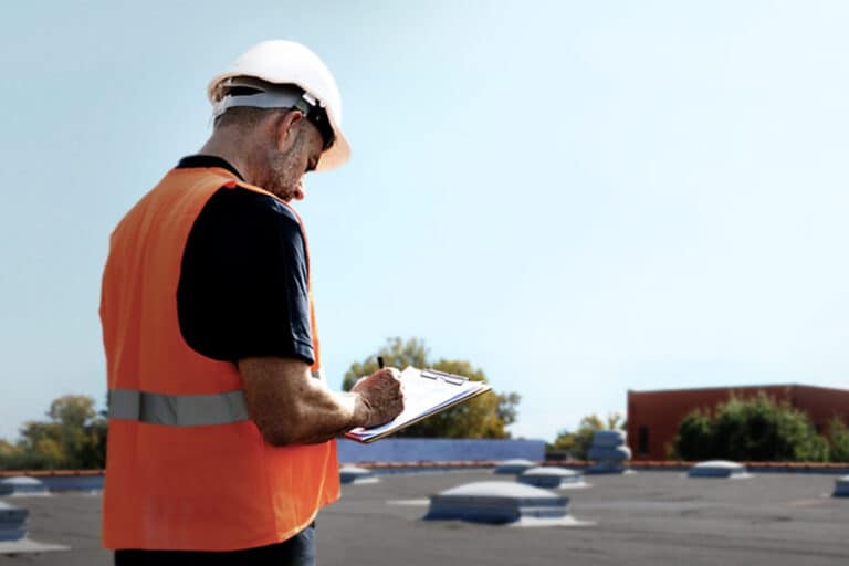 Inspector standing on a commercial roof with a clipboard, conducting an assessment to document roof conditions and identify potential issues.