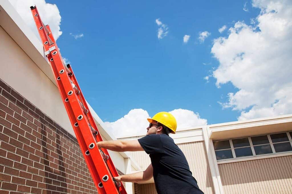 Inspector climbing a ladder to access the top of a commercial roof, preparing to assess its condition and identify potential maintenance needs.