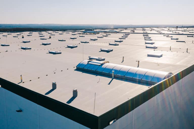 Wide view of an industrial facility with a flat roof, showcasing its expansive surface and rooftop equipment, designed to accommodate heavy-duty operations and withstand industrial demands.