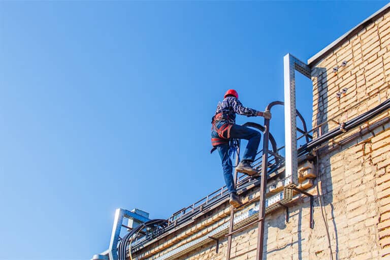 Inspector climbing a ladder to access a commercial roof, demonstrating the importance of regular roof inspections as part of effective roof management to identify potential issues and ensure long-term roof performance.