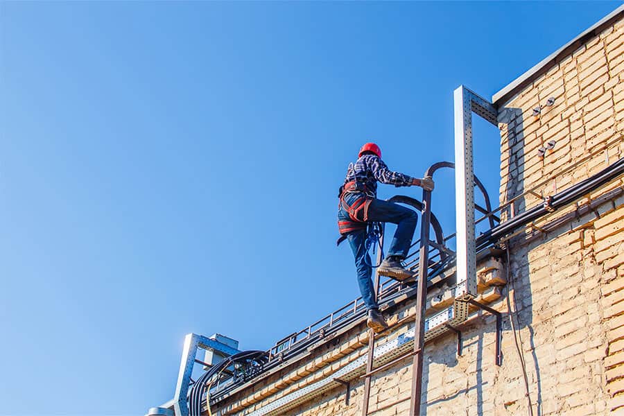Inspector climbing a ladder to access a commercial roof, demonstrating the importance of regular roof inspections as part of effective roof management to identify potential issues and ensure long-term roof performance.