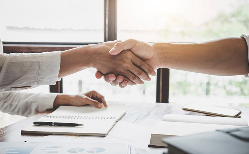 Contractor and business representative shaking hands over a table, symbolizing a successful partnership and agreement for roofing services or projects.