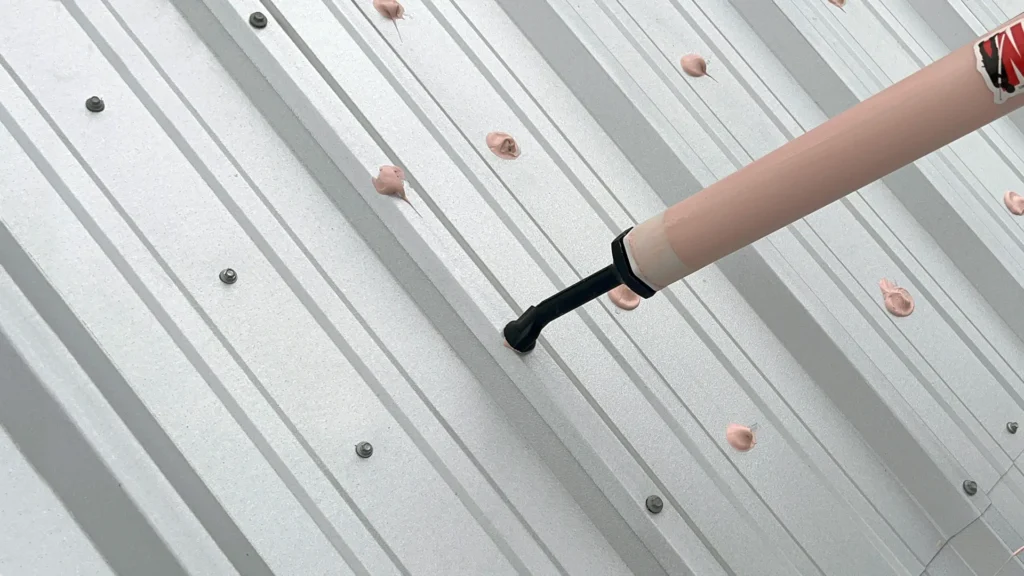 Close-up view of contractor applying pink acrylic roof sealant to fasteners of commercial metal roof