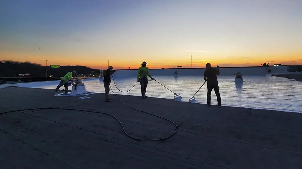 Roofing contractors applying coating to flat roof at dusk