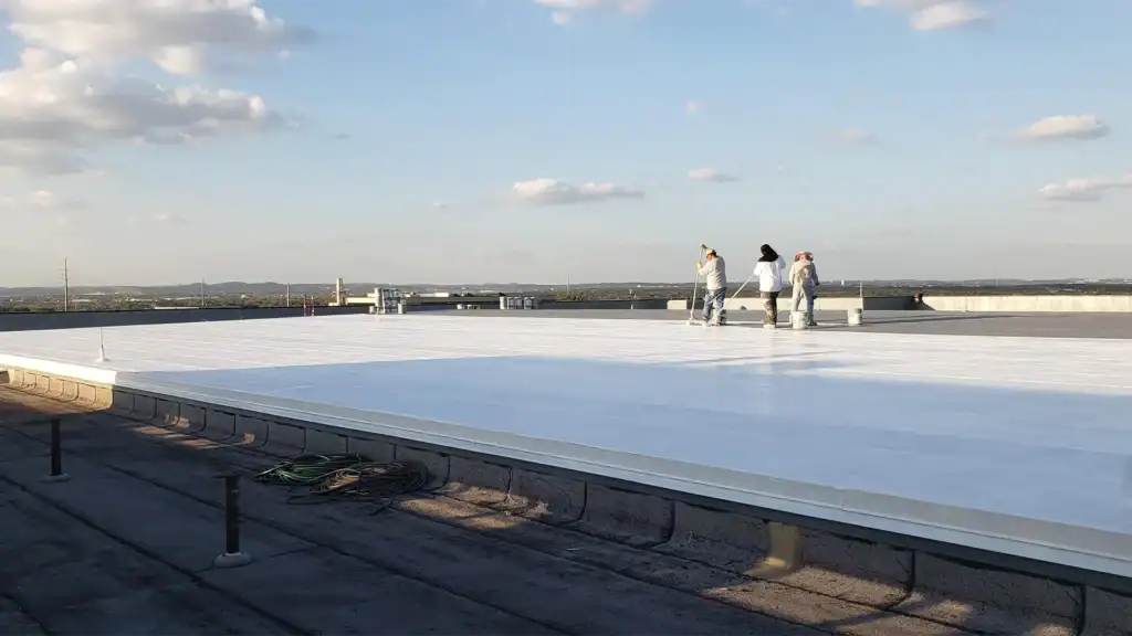 Workers applying roof coating on large flat roof